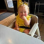 Sage joined the competition — help win amazing prizes! child, toddler, high_chair, yellow_clothing, hair_bows, smiling, indoor, table, snack, baby, seat_belt, wooden_floor, door, window, black_furniture, tile_floor, cute, person, happy, chewing