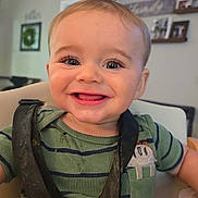 Monty is registered to the contest to win money with this photo: baby, child, smiling, high_chair, green_shirt, striped_clothing, face, eyes, mouth, tongue, hair, indoor, home, furniture, person, cute, happy, seatbelt, feeding, infant