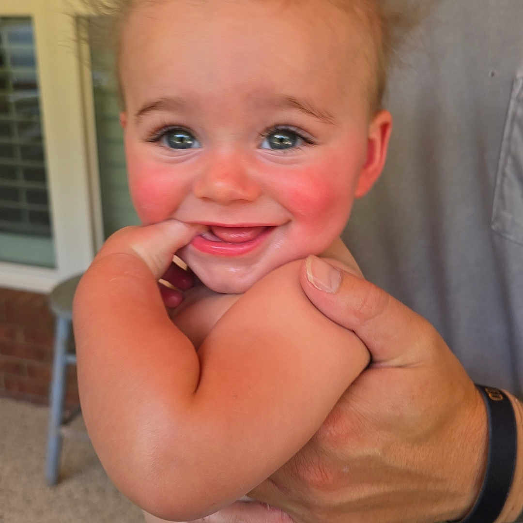 Monty is registered to the contest to win money with this photo: adult_hand, baby, blue_clothing, brick_wall, chair, child, closeup, cute, expression, finger, hair, hand, happy, holding, outdoor, person, porch, skin, smiling, window