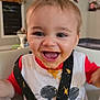 baby, child, high_chair, food, messy, smile, happy, face, bib, indoor, table, cheese, green_beans, person, clothing, red_shirt, white_bib, hair, mouth_open, joy