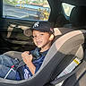 child, boy, car_seat, car_interior, baseball_cap, smile, seatbelt, window, sunlight, shadow, clothing, happy, seat, vehicle, person, casual, transportation, safety, daylight, portrait
