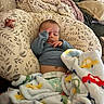 baby, sleeping, blanket, pillow, couch, knitted_throw, diaper, clothing, hand, face, infant, cozy, indoor, resting, peaceful, soft_texture, patterned, colorful, comfort, child