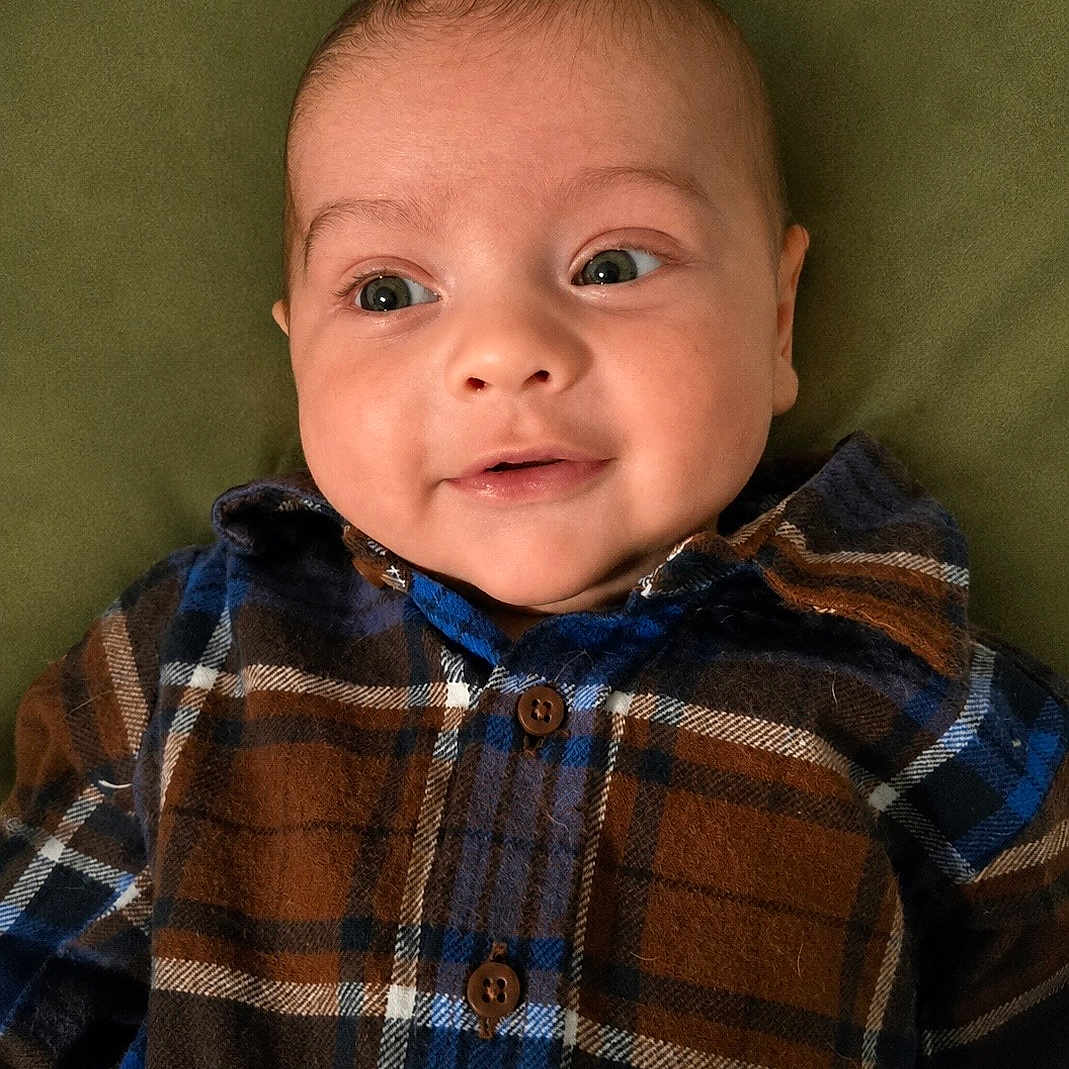 Atlas joined the competition — help win amazing prizes! baby, infant, plaid_shirt, blue, brown, green_background, cute, smile, face, eyes, child, portrait, lying_down, clothing, person, young, skin, head, buttoned_shirt, warm