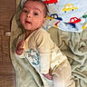 Atlas is registered to the contest to win money with this photo: baby, infant, blanket, onesie, floor, wood_floor, car_pattern, blue, red, yellow, green, soft_texture, child, cute, portrait, laying_down, expression, indoors, person, clothing