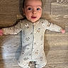 baby, infant, wooden_floor, onesie, bear_pattern, sleepwear, arms_outstretched, cute, child, portrait, indoors, flooring, person, young_child, smiling, head, face, eyes, expression, cozy