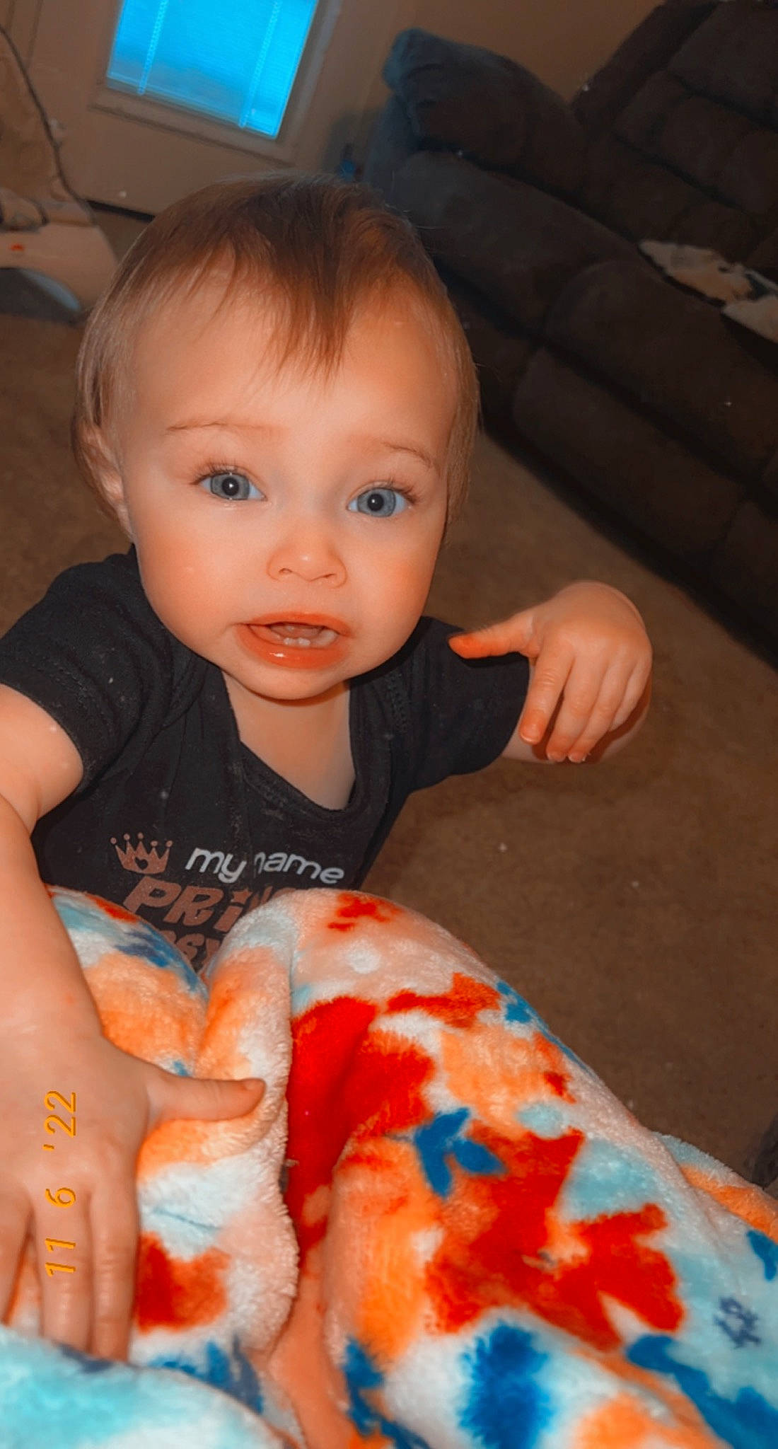 Renesmee is registered to the contest to win money with this photo: baby, baby_toddler_clothing, cheek, child, eye, finger, fun, human_body, iris, lip, mouth, nail, nose, orange, person, sitting, skin, sleeve, surprise, t_shirt