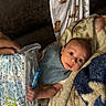 baby, infant, blanket, hand, candy, face, person, cozy, patterned_cloth, animal_print, wrapped, curious, wide_eyes, indoor, soft_texture, protective_hand, packaged_item, laying_down, close_up, young_child