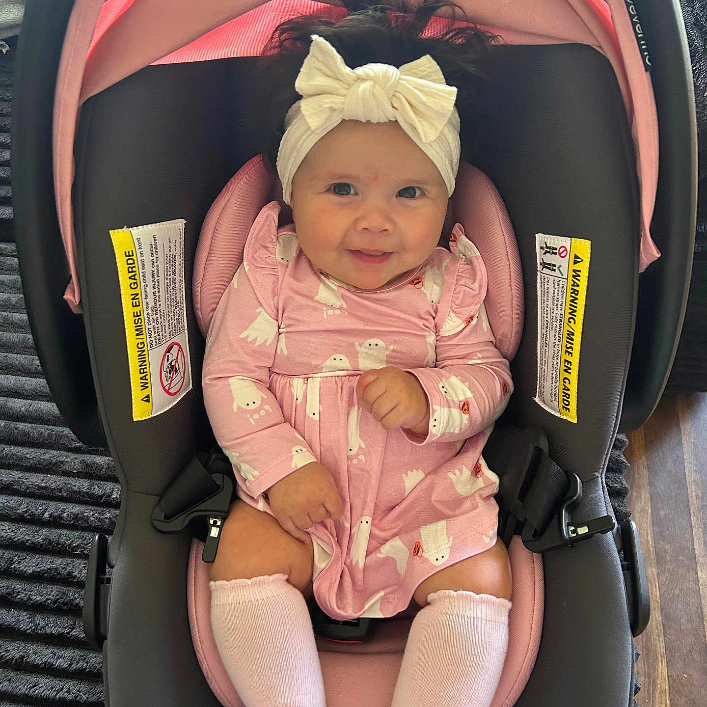 Cecelia is registered to the contest to win money with this photo: baby, infant, child, smiling, portrait, car_seat, pink_outfit, headband, bow, socks, seated, indoor, happy, face, eyes, clothing, baby_carrier, safety_labels, wood_floor, rug