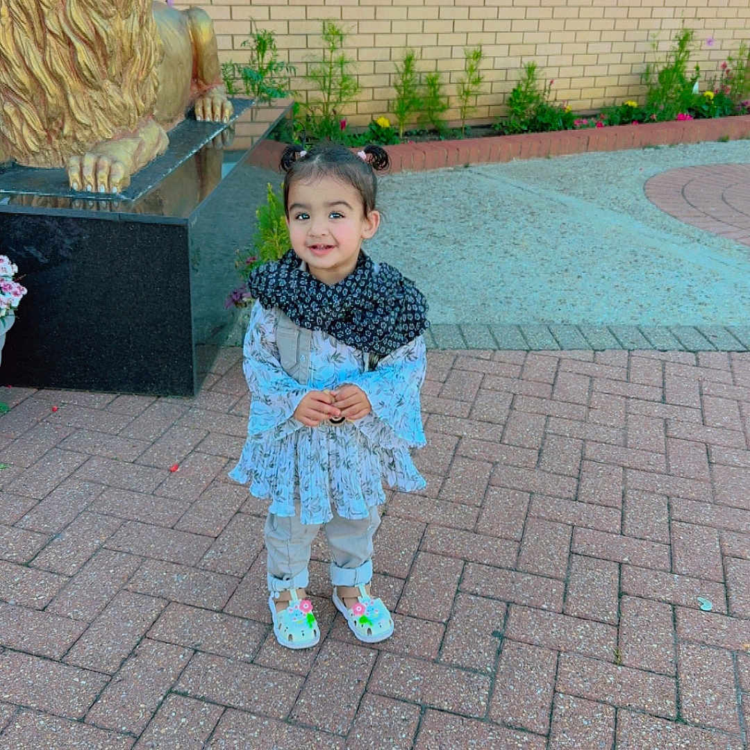 Arveen is registered to the contest to win money with this photo: brick_pavement, building, child, clothing, cute, daylight, flower, happy, lion_statue, nature, outdoor, person, plant, reflection, scarf, shoes, smiling, statue, toddler, window