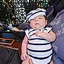 baby, infant, child, striped_clothing, hat, sailor_outfit, person, indoor, table, hand, furniture, stroller, face, cute, chubby, holding, adult_hand, pattern, fabric, portrait