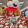 baby, plush_toy, stuffed_animal, beaver, mascot, child, store, retail, toy_display, red_shirt, gray_pants, smiling, indoor, lighting, cute, sitting, shopping, clothing, floor, person