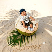 Ignatius joined the competition — help win amazing prizes! baby, child, beach, sand, coconut, blanket, green_leaf, summer, shell, footwear, headwear, toddler, ocean, sky, outdoor, nature, portrait, casual_clothing, sitting, sunlight