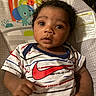 baby, infant, child, curly_hair, striped_shirt, nike_logo, red_logo, baby_seat, animal_print, elephant, monkey, sun, hand, face, eyes, cute, portrait, indoors, colorful, curious