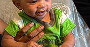 Kysen joined the competition — help win amazing prizes! baby, child, green_clothing, hand, couch, indoor, smiling, person, hair_buns, seated, infant, cute, happy, skin, face, holding, text_on_clothing, adult_hand, fabric, home