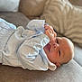 baby, infant, child, blue_clothing, couch, cushion, soft_fabric, indoors, portrait, smiling, tongue_out, relaxed, cute, cozy, young_child, head, face, comfort, lying_down, home