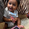 baby, child, infant, sitting, smiling, happy, portrait, face, eyes, hands, couch, cushion, tablet, indoors, home, furniture, patterned_fabric, short_hair, casual_clothing, playtime