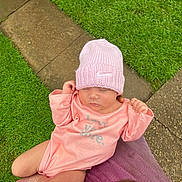 Iraheta is registered to the contest to win money with this photo: baby, infant, pink_hat, pink_onesie, sleeping, outdoor, grass, pathway, person_holding, peaceful, cute, child, knit_hat, soft_lighting, closeup, newborn, toddler, nature, hands, resting