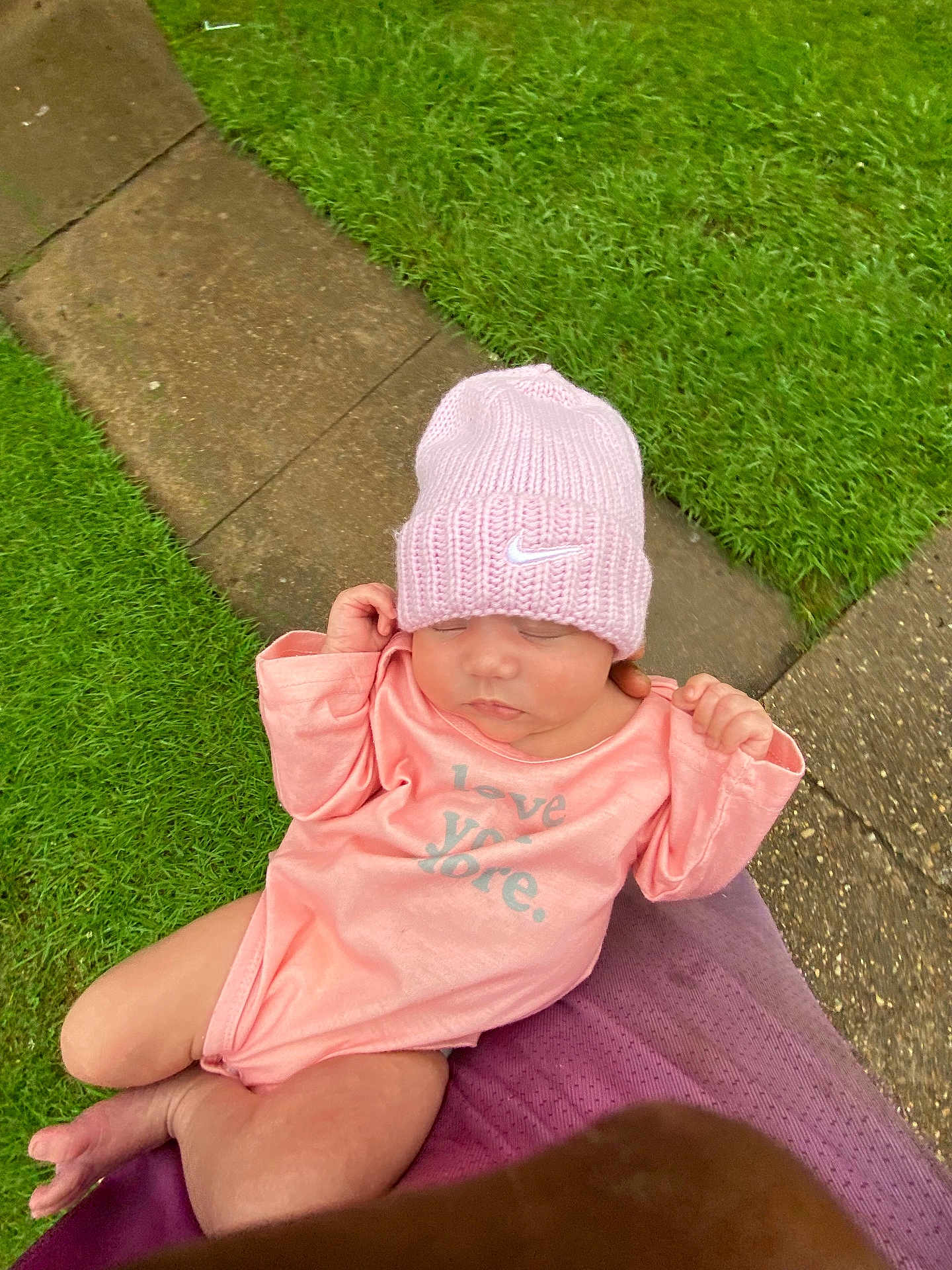 Iraheta is registered to the contest to win money with this photo: baby, infant, pink_hat, pink_onesie, sleeping, outdoor, grass, pathway, person_holding, peaceful, cute, child, knit_hat, soft_lighting, closeup, newborn, toddler, nature, hands, resting