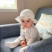 Selene is registered to the contest to win money with this photo: baby, blue_chair, child, cozy, cushion, cute, face, floral_pattern, hat, home, indoor, infant, natural_light, pajamas, person, portrait, sitting, soft_lighting, white_hat, window