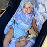 baby, baby_accessories, bib, blanket, blue_outfit, bonnet, bottle, child, clothing, cute, daylight, face, infant, person, portrait, relaxing, soft_toy, stroller, toy, white_socks