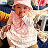 Selene is registered to the contest to win money with this photo: baby, blurred_background, child, cozy, cute, happy, holding, home, indoor, infant, knitted_socks, person, pink_bib, pink_dress, pink_hat, portrait, sitting, soft_lighting, sucking_thumb, warm_colors