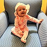 armchair, baby, baby_clothing, blue_chair, child, comfortable, cozy, cute, flamingo_pattern, furniture, happy, hat, indoor, infant, onesie, person, portrait, seated, smiling, toothy_grin