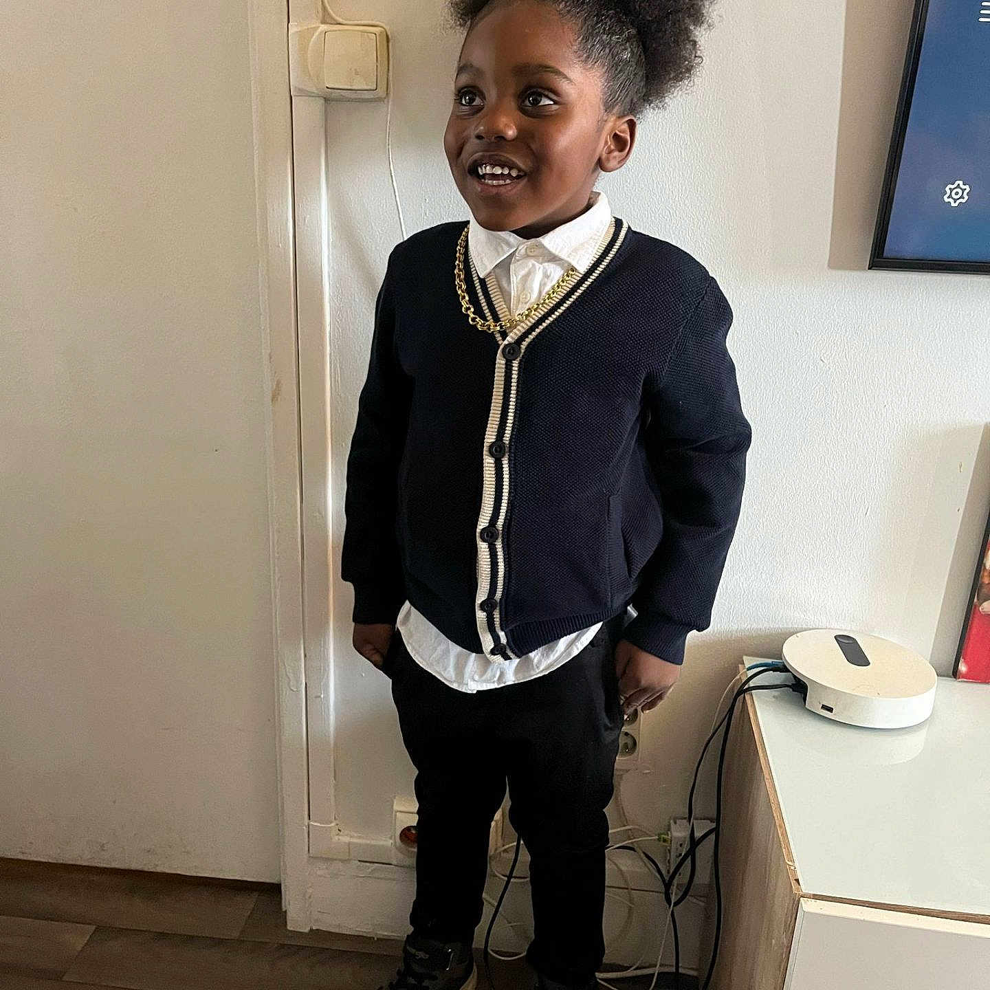 Whayat participe au concours pour gagner de l'argent avec cette photo : afro_hairstyle, cabinet, cardigan, casual, child, device, electrical_outlet, fashion, floor, hair, happy, indoor, pants, person, portrait, smiling, sneakers, standing, wall, white_shirt