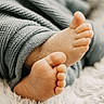 baby_feet, toes, knitted_pants, gray_clothing, close_up, soft_texture, fluffy_surface, infant, cute, cozy, skin, foot, sleepwear, baby, newborn, warm_lighting, relaxation, comfort, small, resting