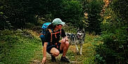 Naïko participe au concours pour gagner de l'argent avec cette photo : adventure, backpack, cap, cliff, crouching, dog, forest, grass, greenery, happy, hiker, husky, nature, outdoor, person, pet, rocks, sunlight, trail, trees
