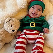 Fabio a rejoint le concours — aidez-le/la à gagner de superbes lots ! baby, infant, smiling, elf_costume, striped_pants, green_top, teddy_bear, soft_toy, blanket, fluffy, cute, happy, holiday, festive, child, portrait, indoors, cozy, playful, lying_down