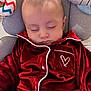 baby, infant, sleeping, closed_eyes, red_pajamas, velvet, heart_patch, head, face, cheeks, cushion, seat, toy, plush_toy, blanket, indoors, portrait, peaceful, soft_texture, young_child