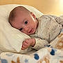 baby, infant, newborn, pillow, blanket, bed, lying_down, portrait, face, eyes, hand, onesie, swaddle, cheek, soft_texture, cozy, indoor, wood_headboard, pattern, cute