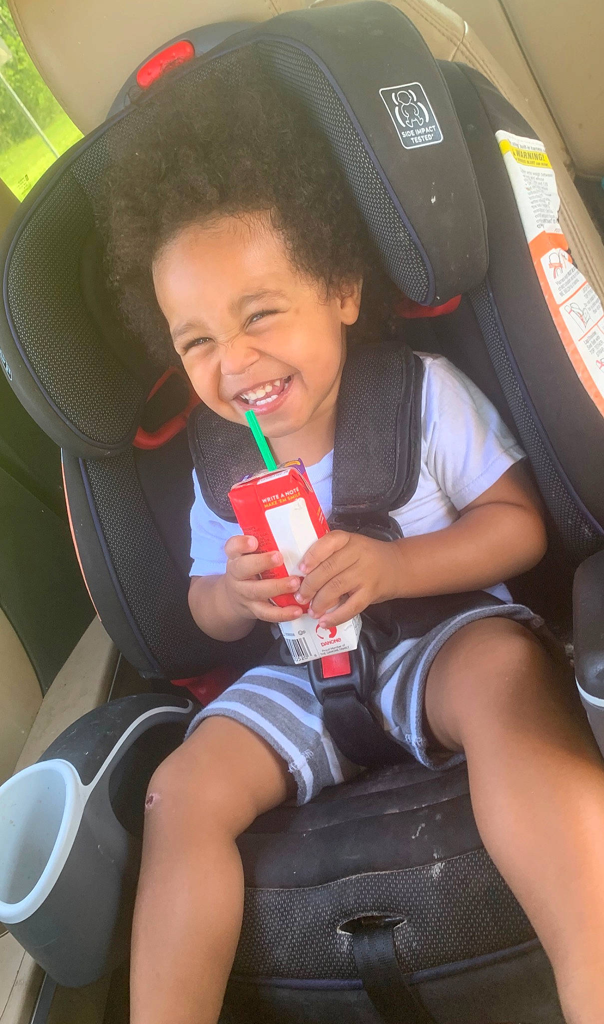 Malachi is registered to the contest to win money with this photo: arm, automotive_design, car_seat, car_seat_cover, chair, clothing, comfort, facial_expression, finger, joy, lap, leg, leisure, person, product, red, skin, smile, steering_wheel, thigh