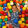 baby, ball_pit, blue_outfit, child, colorful_balls, cute, fun, happy, holding_ball, indoor, infant, joyful, multicolored, patterned_clothing, playful, playtime, portrait, smiling, toddler, young_child