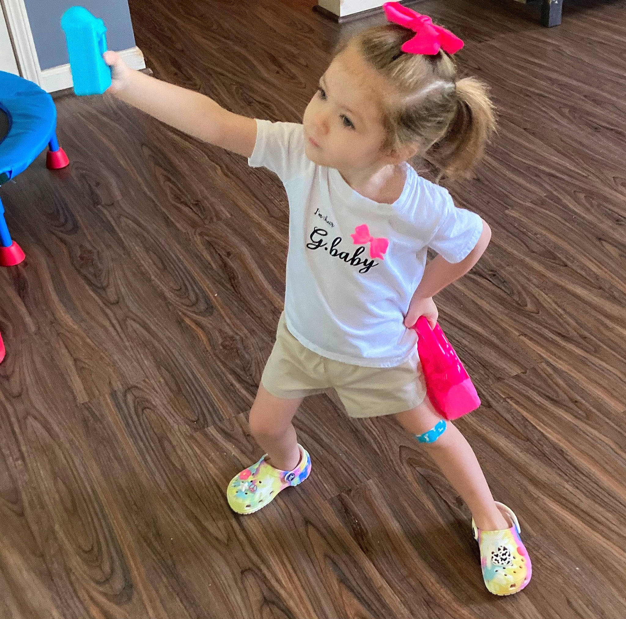 Adalynn is registered to the contest to win money with this photo: baby_toddler_clothing, child, finger, floor, flooring, fun, happy, hardwood, leg, leisure, party_supply, person, pink, shorts, sneakers, sock, t_shirt, thigh, toddler, toy