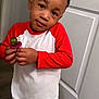 child, boy, indoor, toy, red_shirt, white_shirt, blue_shorts, standing, curious, holding, door, floor, shorts, casual_clothing, young_child, portrait, person, playful, expression, head_tilt