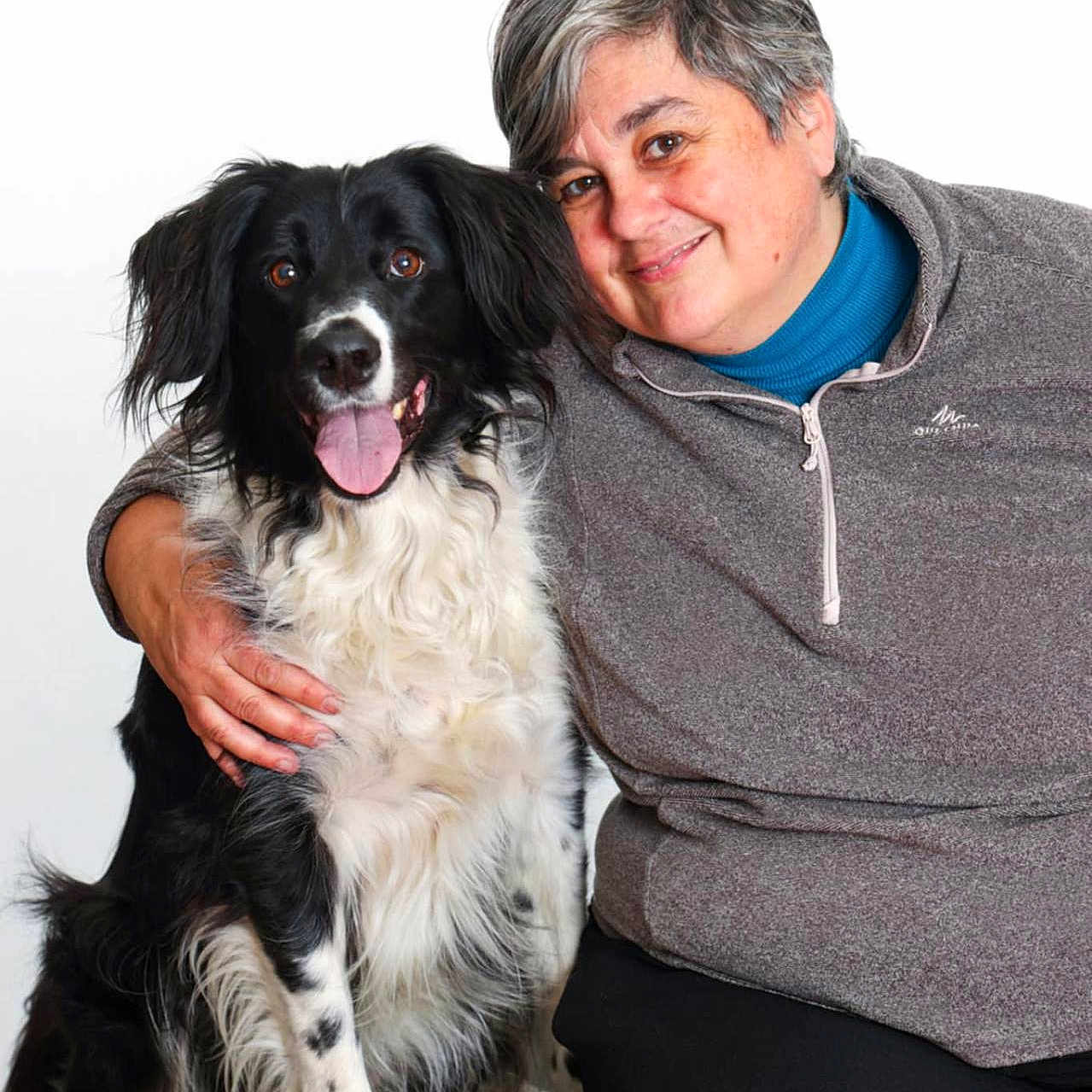 Mina participe au concours pour gagner de l'argent avec cette photo : woman, person, dog, border_collie, black_and_white, fluffy, long_hair, tongue_out, smiling, portrait, companion_animal, pet, cuddling, seated, gray_sweater, blue_shirt, black_pants, white_background, indoor, happy