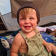 Derek is registered to the contest to win money with this photo: toddler, child, smiling, hat, overalls, tent, camping, outdoor, happy, baby, clothing, portrait, person, fabric, blanket, playful, cute, nature, daylight, seated
