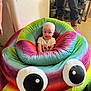 baby, child, plush, rainbow, colorful, indoor, furniture, funny, smiling, person, seat, toy, googly_eyes, cozy, happy, cushion, casual_clothing, floor, adult, legs