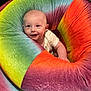 baby, infant, smile, face, child, colorful, plush, rainbow, soft, cushion, seated, happy, indoors, comfort, cute, bright, young, person, cozy, playful