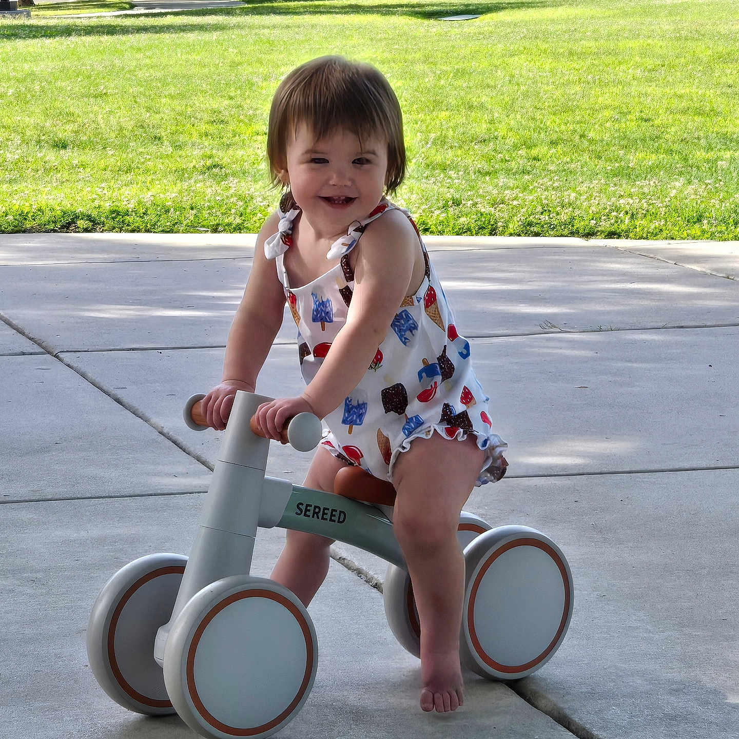 Bailey Mae joined the competition — help win amazing prizes! balance_bike, barefoot, child, cute, daytime, grass, happy, nature, outdoor, park, person, play, romper, sidewalk, smiling, summer, sunlight, toddler, toy, trees