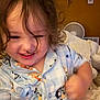 toddler, child, curly_hair, pajamas, smiling, indoor, bed, blanket, motion_blur, face, happy, furniture, home, person, cozy, cute, clothing, portrait, young_child, room