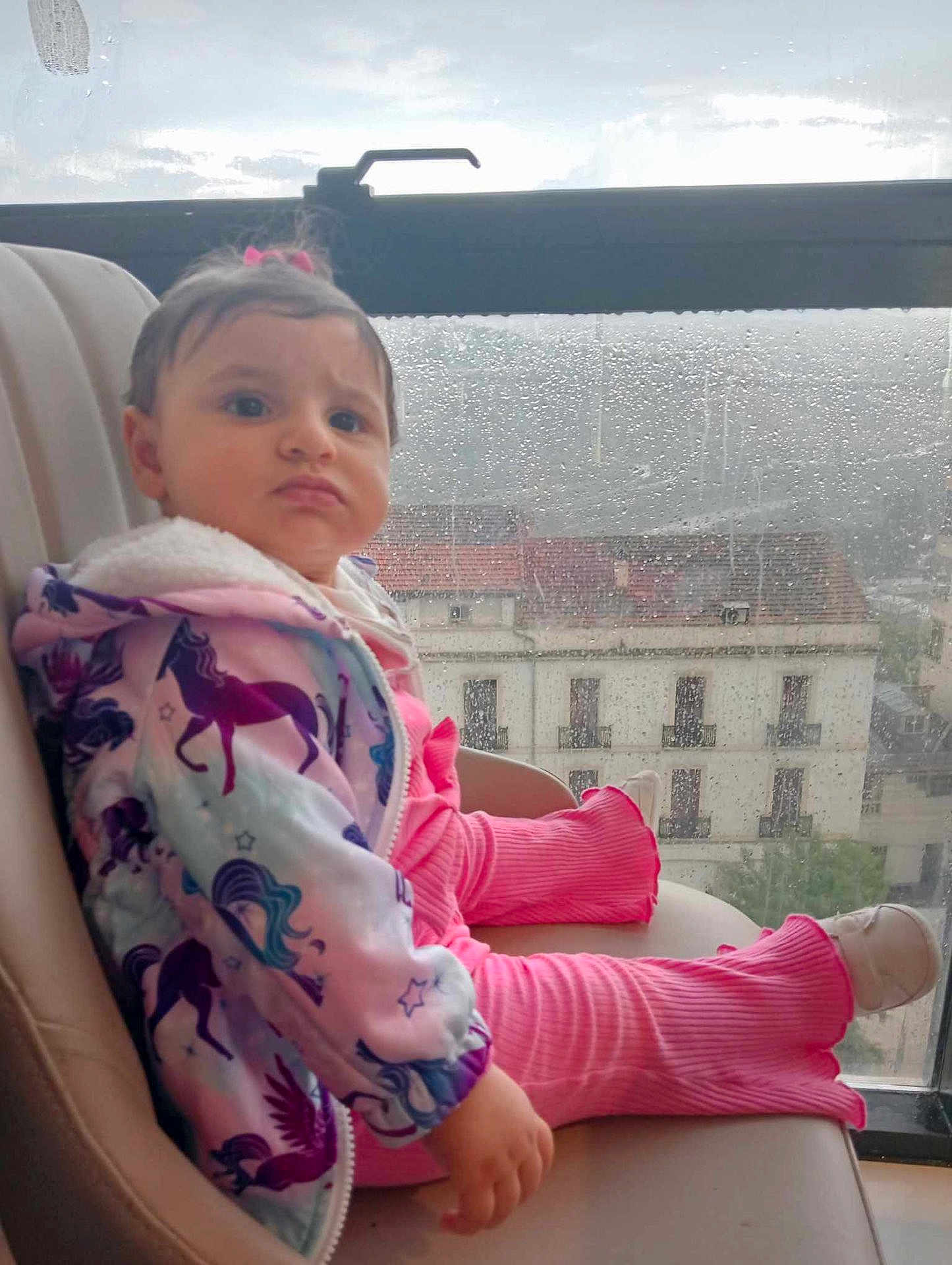 Loujayne participe au concours pour gagner de l'argent avec cette photo : toddler, child, rain, window, chair, pink_clothing, unicorn_pattern, jacket, pout, indoor, gloomy_weather, raindrops, building_outside, curly_hair, footwear, casual_clothing, portrait, seated, expression, young_child