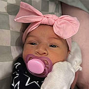 Renesmee joined the competition — help win amazing prizes! baby, infant, child, portrait, headband, pink_bow, pacifier, mitten, black_outfit, star_pattern, lying_down, bed, blanket, checkered_blanket, indoor, close_up, face, awake, cute, parent_arm