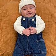 Beau is registered to the contest to win money with this photo: baby, smiling, white_hat, knitwear, denim_overalls, hands, orange_blanket, cozy, infant, cute, child, portrait, lying_down, clothing, warm, face, headwear, happy, baby_booties, texture