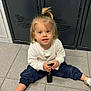 casual_clothing, child, curious, floor, flooring, gold_shoes, hair, indoor, keys, locker, looking_at_camera, navy_pants, person, ponytail, sitting, small_hands, tiles, toddler, white_sweater, young_child