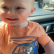 David is registered to the contest to win money with this photo: baby, child, smiling, orange_clothing, cartoon, crocodile, van, vehicle, car_interior, sunlight, portrait, cute, happy, infant, face, seat, window, daylight, young_child, casual
