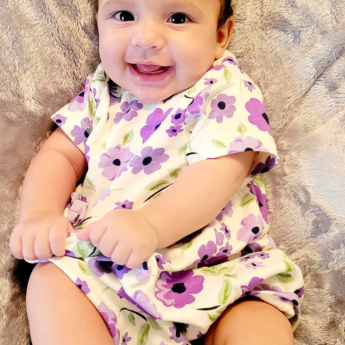Josslyn is registered to the contest to win money with this photo: adorable, baby, child, closeup, curly_hair, cute, face, feet, hand, happy, indoors, infant, playful, portrait, purple_flower_dress, sitting, smiling, soft_blanket, white_socks, young_child