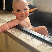 Lily is registered to the contest to win money with this photo: baby, bathtub, water, child, smile, blue_eyes, skin, wet_hair, arm, relaxing, natural_light, bathroom, wood, edge, infant, cute, portrait, happy, young_child, indoors