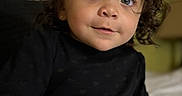 Amari joined the competition — help win amazing prizes! child, toddler, portrait, curly_hair, face, eyes, looking_at_camera, black_clothing, sitting, bed, bedroom, indoor, close_up, photography, serious_expression, cute, dark_clothing, brown_hair, soft_lighting, home